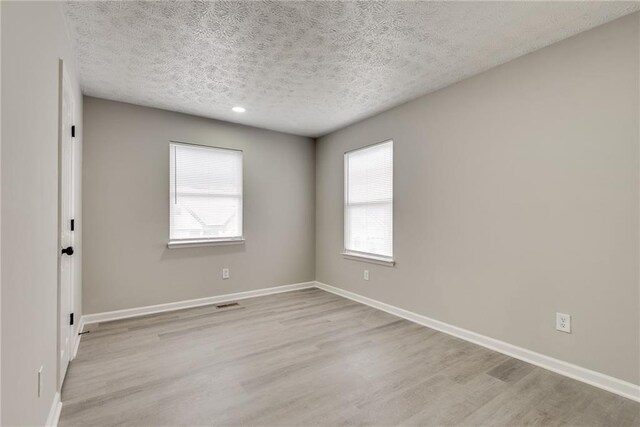 empty room featuring plenty of natural light, a textured ceiling, and light hardwood / wood-style flooring