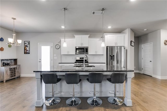 kitchen featuring a center island with sink, sink, stainless steel appliances, and dark stone counters