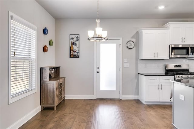 kitchen with appliances with stainless steel finishes, wood-type flooring, backsplash, white cabinetry, and hanging light fixtures