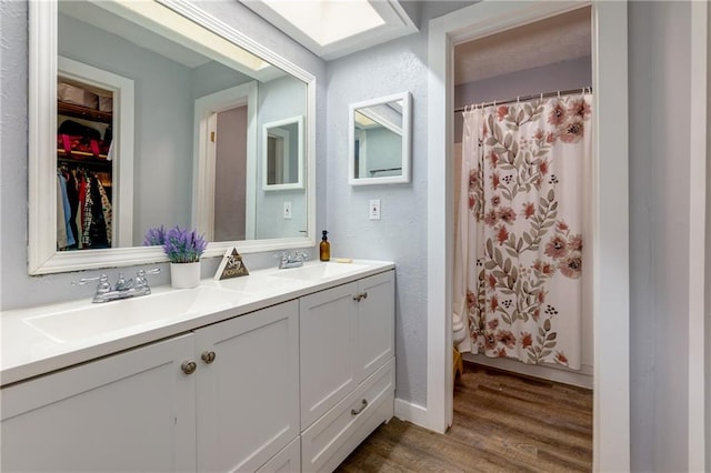 bathroom featuring a skylight, double vanity, a sink, and wood finished floors