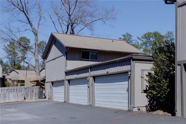 garage featuring driveway, central air condition unit, and fence