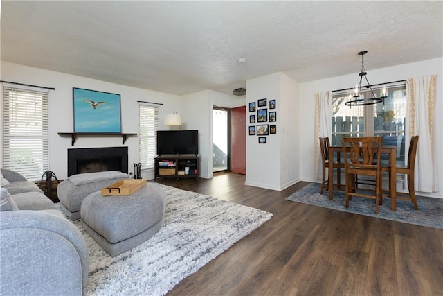 living room with baseboards, dark wood-style flooring, a textured ceiling, a fireplace, and a notable chandelier