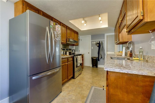 kitchen featuring a tray ceiling, stainless steel appliances, a textured ceiling, under cabinet range hood, and a sink