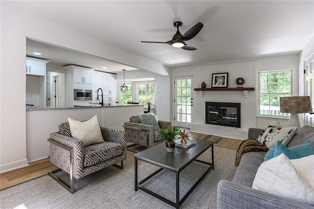 living room with ceiling fan, sink, light wood-type flooring, and a fireplace