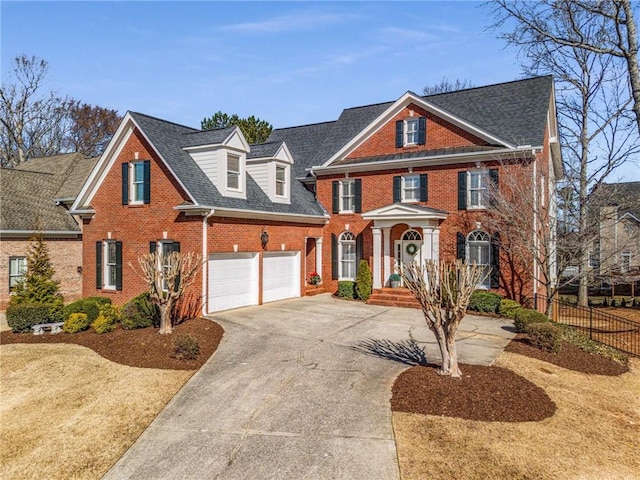 colonial house featuring a garage, brick siding, fence, driveway, and roof with shingles