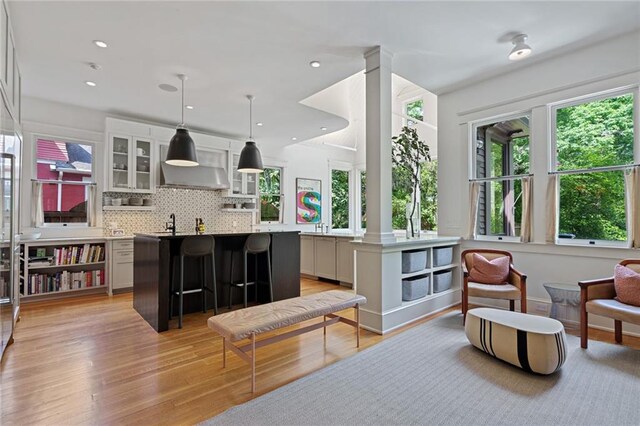 interior space with ornate columns, wall chimney exhaust hood, tasteful backsplash, light wood-style flooring, and decorative light fixtures
