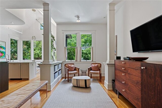 living area featuring ornate columns, lofted ceiling, and light wood-style floors