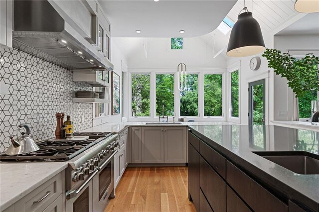 kitchen featuring light stone countertops, a sink, wall chimney exhaust hood, range with two ovens, and tasteful backsplash