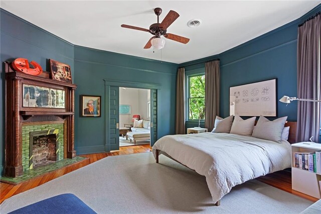 bedroom with visible vents, a fireplace with flush hearth, ceiling fan, and wood finished floors