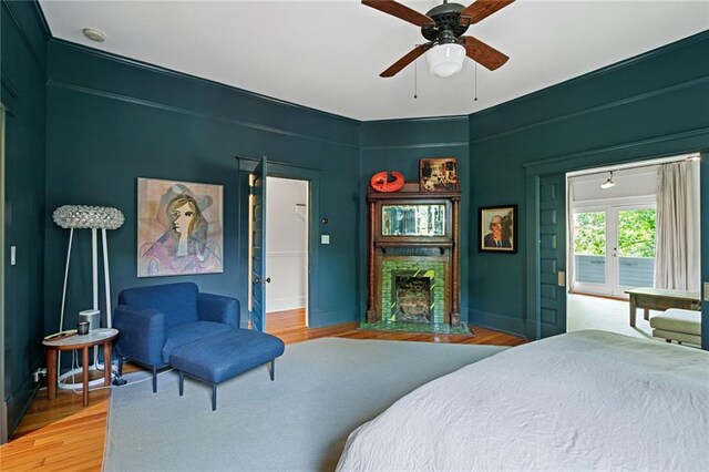 bedroom featuring ceiling fan, access to exterior, light wood-style flooring, baseboards, and a fireplace with flush hearth