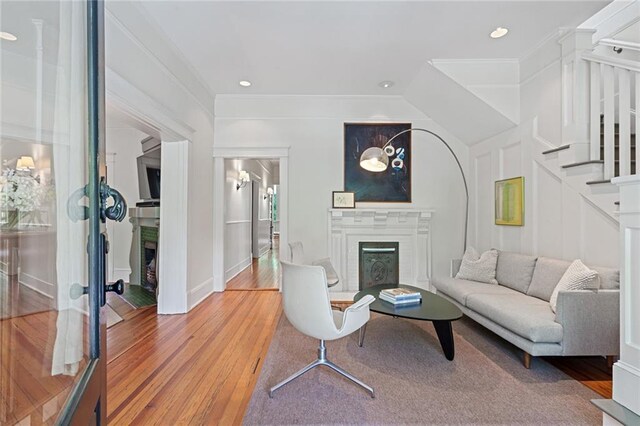 living area with crown molding, light wood finished floors, a fireplace, stairs, and recessed lighting