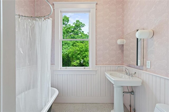 full bathroom with wainscoting, a healthy amount of sunlight, and wallpapered walls
