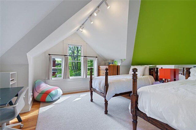 bedroom with track lighting, wood finished floors, and vaulted ceiling