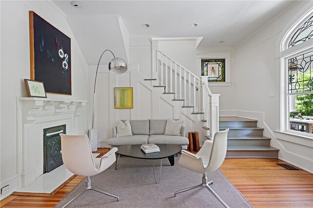 living area featuring a fireplace, wood finished floors, stairway, ornamental molding, and a decorative wall