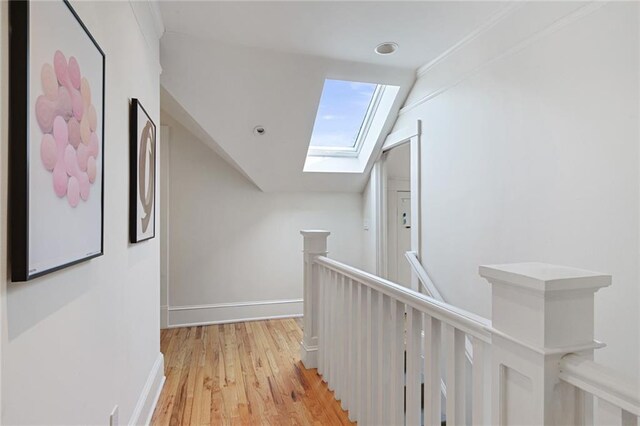 corridor featuring baseboards, light wood finished floors, vaulted ceiling with skylight, and an upstairs landing