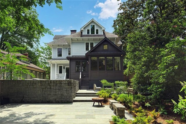 view of front of house with a shingled roof, a chimney, and a sunroom