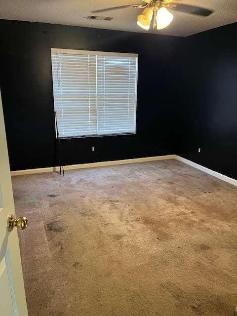 carpeted empty room with visible vents, a ceiling fan, and baseboards