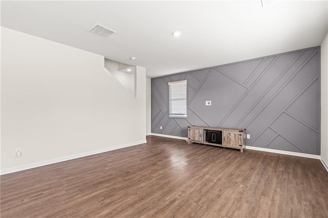 unfurnished living room with baseboards, wood finished floors, visible vents, and a decorative wall