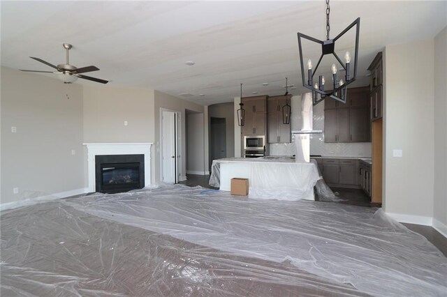 kitchen featuring stainless steel microwave, a kitchen island, tasteful backsplash, open floor plan, and wall chimney range hood