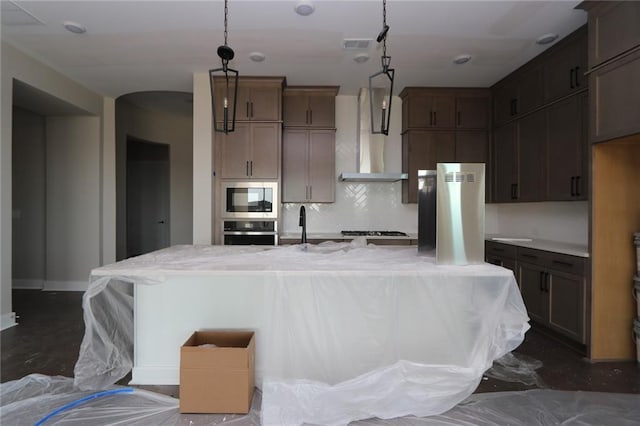 kitchen featuring visible vents, a spacious island, stainless steel appliances, wall chimney exhaust hood, and tasteful backsplash