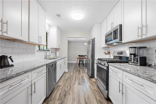 kitchen featuring light wood-type flooring, a sink, baseboards, white cabinets, and stainless steel appliances
