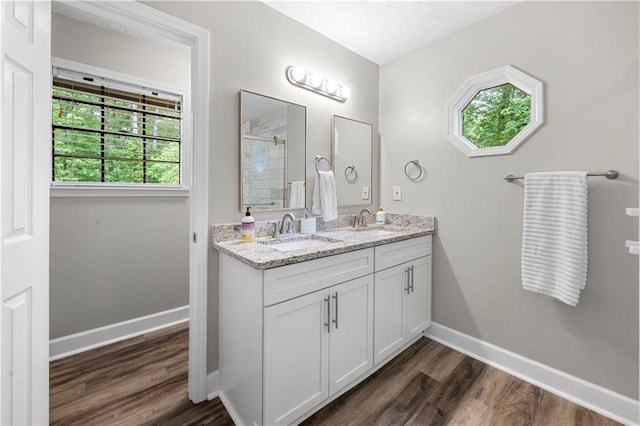 bathroom with a sink, baseboards, a tile shower, and wood finished floors