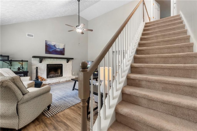 staircase with visible vents, wood finished floors, a fireplace, ceiling fan, and vaulted ceiling