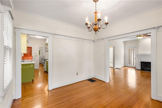 unfurnished dining area featuring a chandelier, light wood-style floors, a fireplace, crown molding, and baseboards
