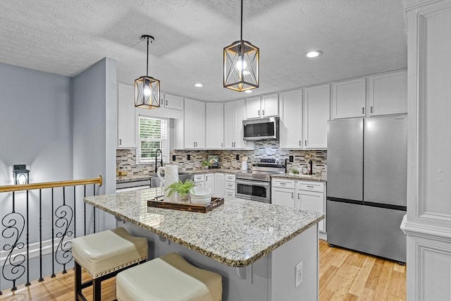 kitchen featuring light stone counters, backsplash, light wood-style flooring, appliances with stainless steel finishes, and white cabinetry