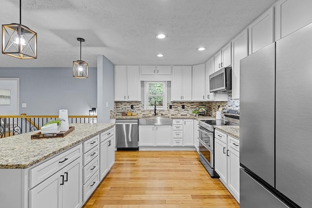 kitchen featuring light wood finished floors, backsplash, appliances with stainless steel finishes, white cabinets, and a sink