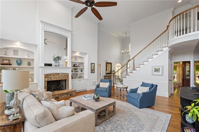 living room featuring ceiling fan, stairway, a towering ceiling, wood finished floors, and built in features