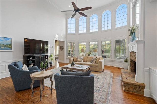 living area with a towering ceiling, ceiling fan, healthy amount of natural light, crown molding, and a fireplace