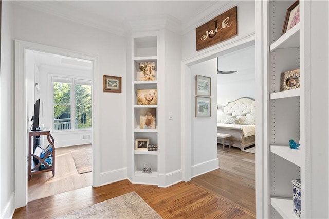 mudroom with built in features, ornamental molding, wood finished floors, and baseboards