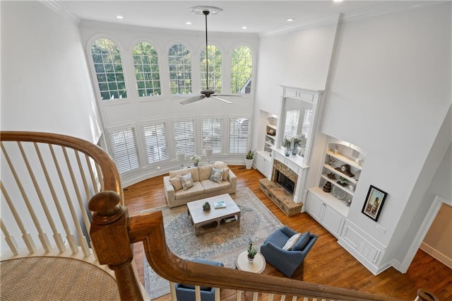 living area featuring built in features, a towering ceiling, ceiling fan, a fireplace with raised hearth, and light wood-style floors