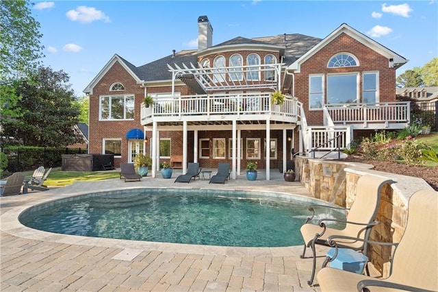 rear view of property featuring a covered hot tub, brick siding, a patio area, and a chimney