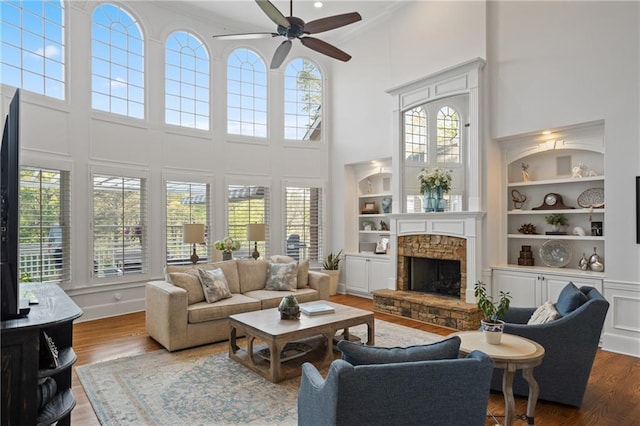 living room with a high ceiling, wood finished floors, plenty of natural light, ceiling fan, and crown molding