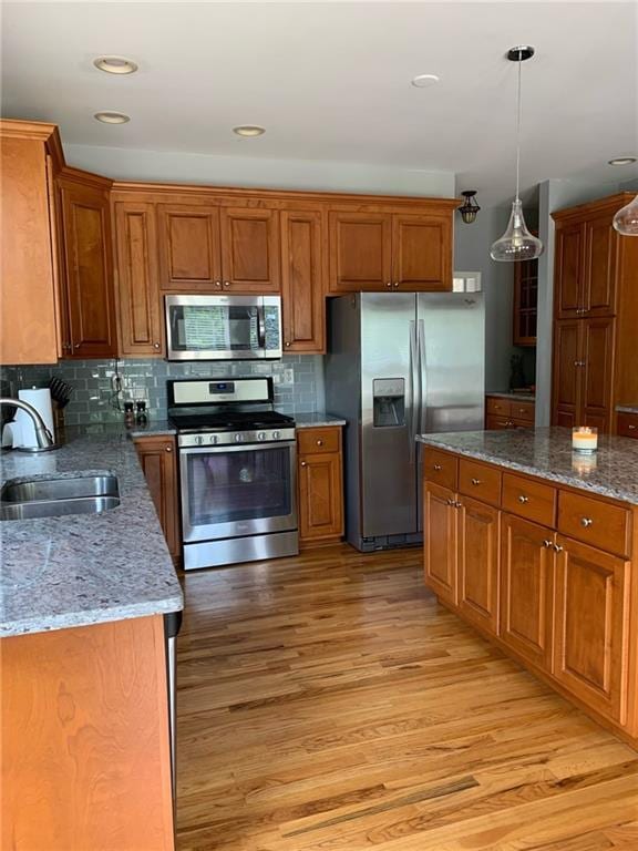 kitchen with appliances with stainless steel finishes, sink, light hardwood / wood-style flooring, and decorative light fixtures