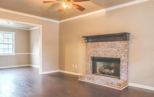 unfurnished living room featuring a fireplace, dark wood-type flooring, ceiling fan, and crown molding