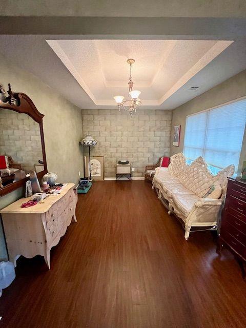 living area featuring a raised ceiling, dark wood-type flooring, and a notable chandelier