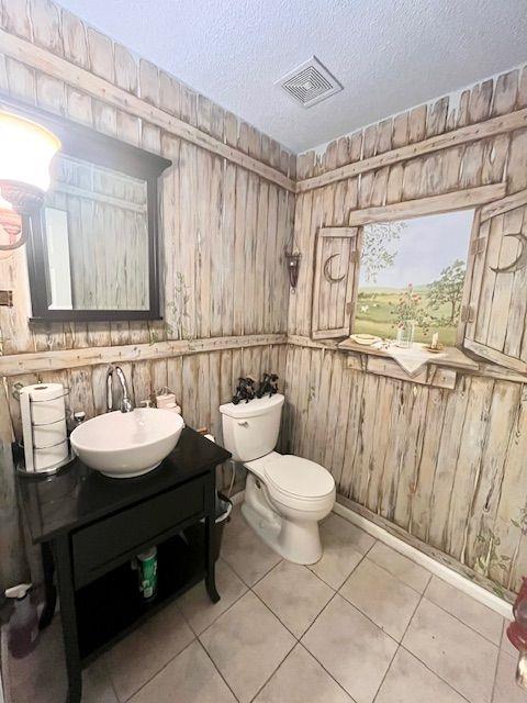 bathroom with tile patterned floors, wooden walls, a textured ceiling, and toilet