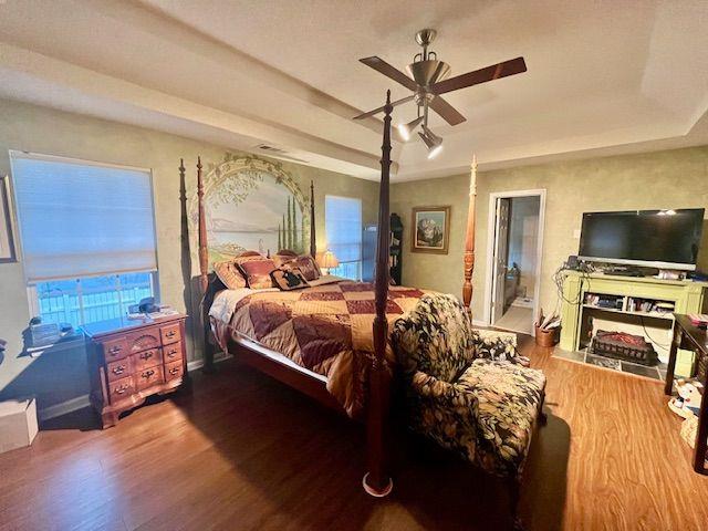 bedroom featuring wood-type flooring, a tray ceiling, ceiling fan, and ensuite bathroom