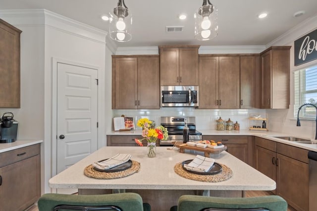 kitchen featuring a sink, tasteful backsplash, stainless steel appliances, a breakfast bar area, and hanging light fixtures