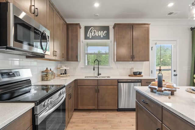 kitchen with tasteful backsplash, light wood finished floors, ornamental molding, appliances with stainless steel finishes, and a sink