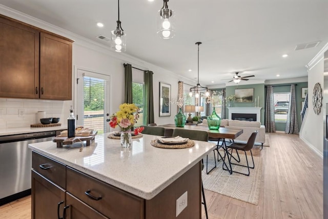 kitchen with light wood-type flooring, a fireplace, dishwasher, crown molding, and tasteful backsplash