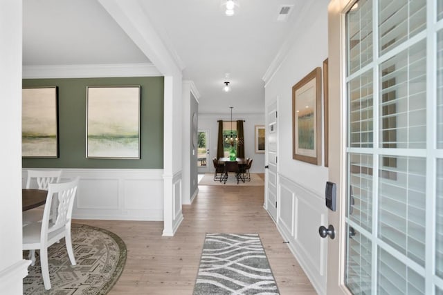 foyer featuring visible vents, light wood finished floors, ornamental molding, and a decorative wall