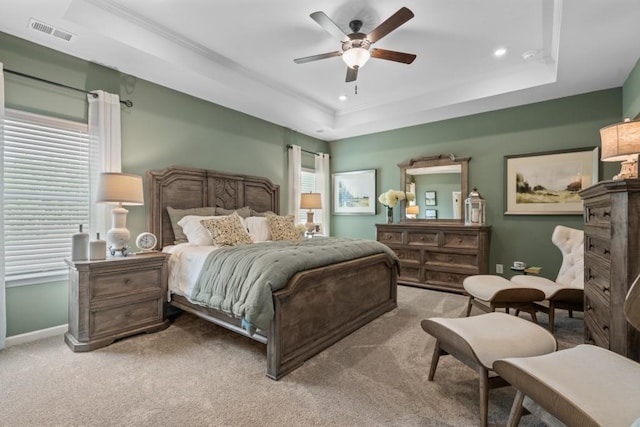 carpeted bedroom with a ceiling fan, baseboards, visible vents, a tray ceiling, and ornamental molding