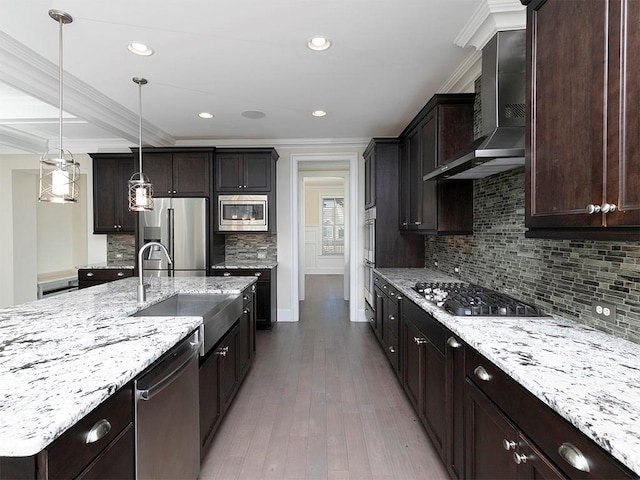 kitchen featuring sink, wall chimney exhaust hood, hardwood / wood-style floors, decorative light fixtures, and appliances with stainless steel finishes