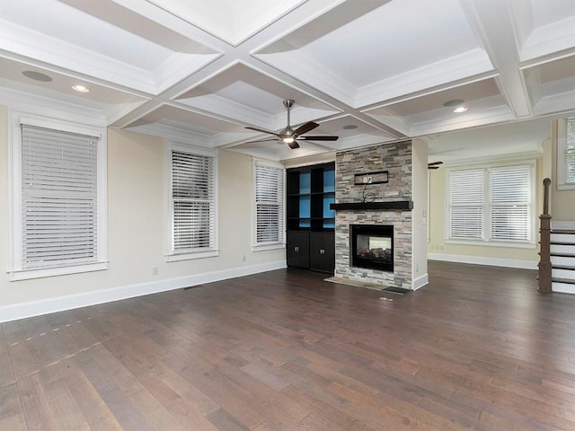 unfurnished living room with beam ceiling, ceiling fan, dark wood-type flooring, coffered ceiling, and a stone fireplace