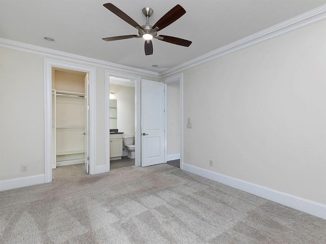 unfurnished bedroom featuring light carpet, ensuite bathroom, crown molding, ceiling fan, and a spacious closet