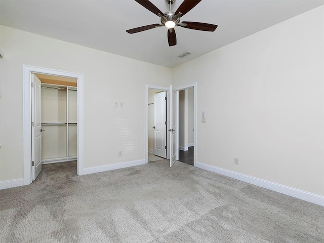 unfurnished bedroom featuring light carpet, a closet, a spacious closet, and ceiling fan